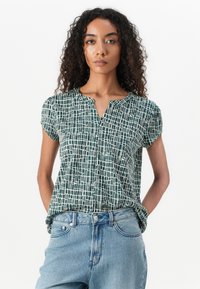 Korte mouwen blouse in groen met een wit ruitpatroon, voorzien van een notch-kraag en lichtgewicht stof. Gecombineerd met een blauwe high-waisted jeans.