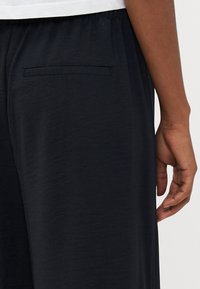 Pantaloni larghi di colore blu scuro realizzati in un tessuto morbido, con vita elasticizzata e una sola tasca posteriore dal design elegante.