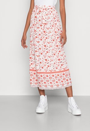 Kvinde iført en hvid midi-nederdel med orange blomsterprint, bølget kant og et bånd spændt om taljen, kombineret med hvide platform-sneakers.