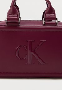 Tume burgundi nahkstoot valgega, millel on kaks käepidet ja eesmisel paneelil suured järgnenud "cK" logod.