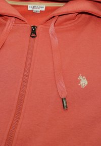 Felpa con zip corallo, in cotone, caratterizzata da una texture fine, zip frontale e logo ricamato. Fila con estremità metalliche.