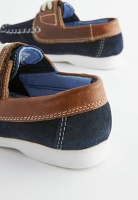 Marineblaue Wildlederschuhe mit braunen Lederakzenten, weißen Gummisohlen, kontrastierendem Nähen und einem weichen blauen Futter. Design mit abgerundeter Spitze.