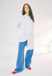 Camicia bianca con colletto e chiusura a bottoni, abbinata a jeans in denim blu a gamba larga e scarpe rosse. Tessuto morbido con una vestibilità rilassata.