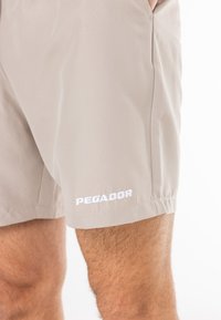 Šviesiai rudos šortai, pagaminti iš lengvos medžiagos, su paprastu dizainu. Baltas „PEGADOR“ logotipas apačioje, su šoninėmis kišenėmis.