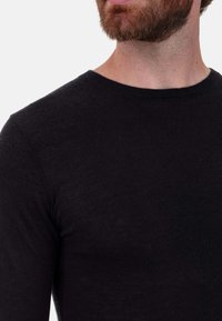 Schwarzes Strickshirt mit langen Ärmeln und Rundhalsausschnitt, das eine glatte Textur und eine enganliegende Passform aufweist, teilweise an einer Schaufensterpuppe oder Person gezeigt.