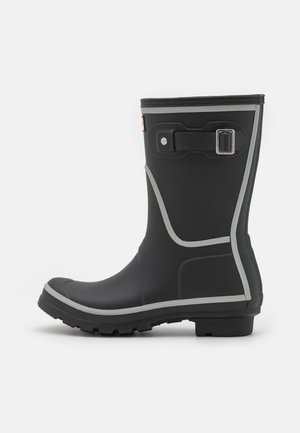 Botte de pluie en caoutchouc noire mi-mollet avec une sangle à boucle argentée et une finition gris clair, semelle robuste, vue de côté sur fond blanc.