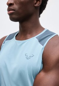 Κοντινό πλάνο άντρα που φοράει ανοιχτό μπλε αμάνικη αθλητική μπλούζα με μικρό λογότυπο ζώου στο στήθος.