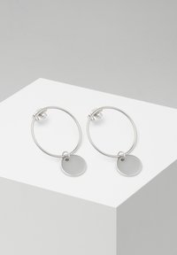 Silberne Creolen mit einem glatten, runden Anhänger, der an jeder hängt, mit einer polierten Oberfläche und minimalistischen Design.