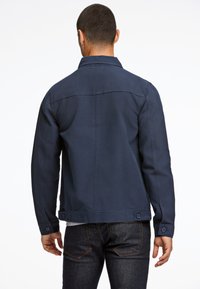 Marineblauwe denimjas met een aansluitende pasvorm, knoopaccenten op de mouwen en een gladde textuur. Heeft een rug yoke voor een gestructureerd ontwerp.