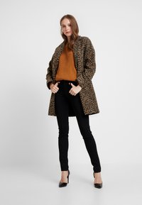 Manteau imprimé léopard, pull jaune moutarde à côtes, jeans noirs et escarpins ; présente une coupe décontractée et des textures remarquables.