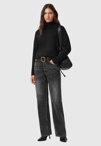 Suéter negro de cuello alto con puños acanalados, jeans gris de pierna ancha, cinturón negro con hebilla cuadrada y un bolso negro desaliñado. Zapatos negros de tacón.