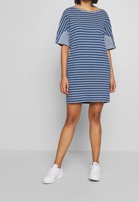 Vestido a rayas en colores azul y blanco, de corte holgado, con mangas anchas y escote redondeado. El tejido parece suave y tiene un diseño casual.