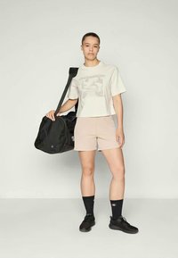 T-shirt cropped de manga curta, bege claro, com estampa gráfica; calções rosa claro; sapatos de treino pretos; mala preta com alça para ombro; meias escuras.