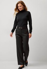 Un maglione a collo alto nero abbinato a pantaloni neri a vita alta e gamba larga. Presenta una cintura elegante con una fibbia argentata e scarpe nere flat.
