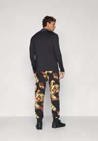 Long-sleeve black top paired with colorful graphic sweatpants featuring a bold face design, primarily black with accents of red and yellow.