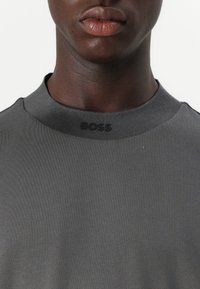 Grå crew-neck t-skjorte laget av glatt bomullsstoff, med en subtil ribbet tekstur og en hevet "BOSS"-logo på kragen.