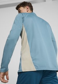Camicia a maniche lunghe azzurro chiaro con un design testurizzato su un braccio e un pannello crema sul lato. Tessuto liscio con una forma aderente.