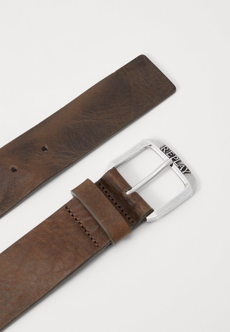 Cinturón de cuero marrón con una hebilla rectangular de plata con "REPLAY" grabado. Superficie texturizada, siete agujeros para ajuste de tamaño.