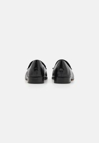 Chaussures habillées en cuir noir avec une finition brillante, petit talon noir, et bout arrondi, présentant des coutures discrètes et une texture lisse.