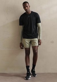 Black short-sleeve athletic shirt, light green long sleeves, beige shorts, black sneakers, and socks with white accents. Smooth fabric texture.