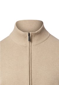 Beige sweater met ritssluiting, hoge geribbelde kraag en gestructureerde stof. Voorzien van een rits aan de voorkant en een gladde afwerking, geschikt om mee te laagjes te dragen.