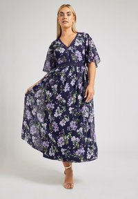 Maxime dress in navy with a floral pattern in purple and green. Transparent fabric, V-neckline, and flutter sleeves. Adjustable waist.