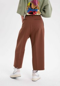 Bruna vida byxor med slät textur, parat med en l�ös grön topp som har en färgglad grafisk design. Vita högskurna sneakers ingår.