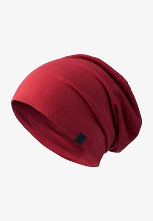 Crvena rastezljiva beanie kapa od mekog materijala, sa ležernim dizajnom i nabranom teksturom, na strani ima malu crnu oznaku s logotipom.