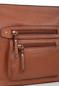 Borsa a mano in pelle marrone con due tasche con zip dotate di hardware dorato, tiranti decorativi e logo del marchio impresso. Texture liscia, forma rettangolare.