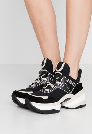 Baskets compensées épaisses noires et beiges avec lacets portées aux pieds sur un fond neutre, montrant les vues latérale et avant.