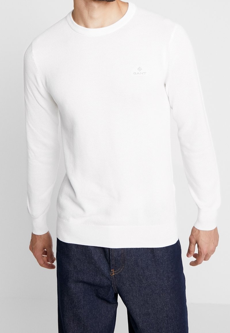 Weißer langärmliger Strickpullover mit Rundhalsausschnitt und dezentem GANT-Logo. Strukturiertes Material, taillierte Passform sowie gerippte Bündchen und Saum.