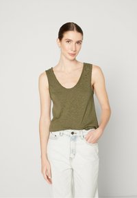 Olive green tank top with a scoop neckline and textured fabric, paired with high-waisted light blue jeans.