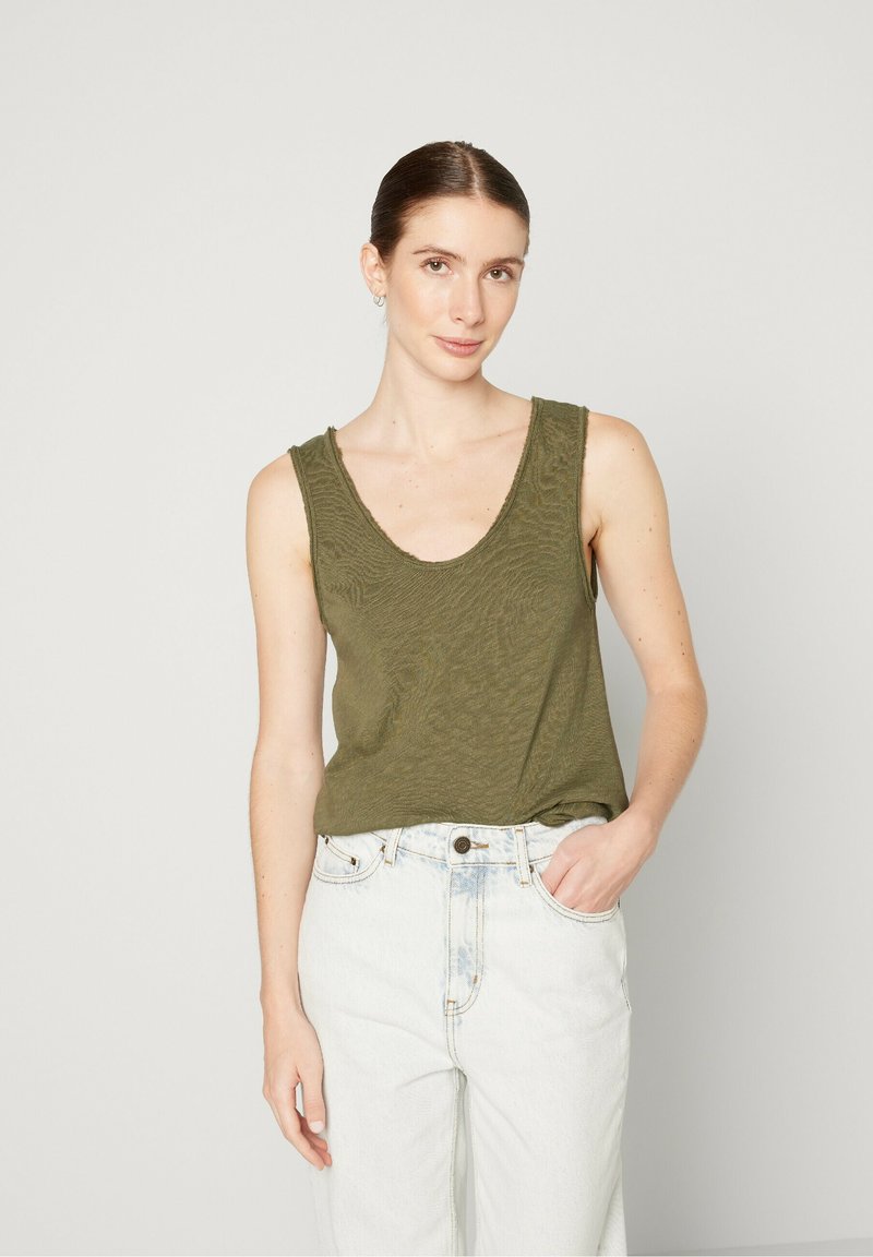 Olive green tank top with a scoop neckline and textured fabric, paired with high-waisted light blue jeans.