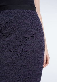 Fialová krajková sukně s květinovými vzory, s hladkým pásem. Textura je složitá, zvýrazňuje hloubku a detaily krajkového designu.