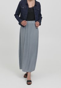 Jeansjacka över en svart spetslinne, kombinerat med en lång mönstrad kjol i marinblått och vitt. Svarta slip-in sandaler kompletterar outfiten.