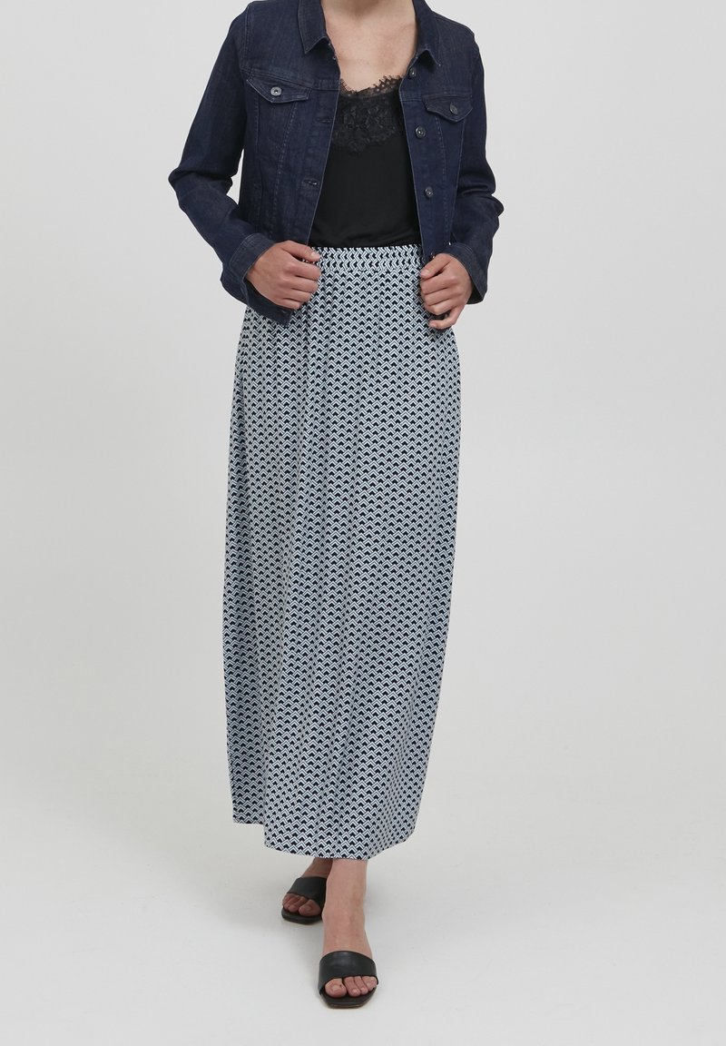 Jeansjacka över en svart spetslinne, kombinerat med en lång mönstrad kjol i marinblått och vitt. Svarta slip-in sandaler kompletterar outfiten.