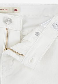 Valge teksariie kuldse tõmbluku ja nööpkinni kinnitusega. Omab kontrastset õmblust ja brändimärki, esitledes klassikalist avarust.