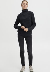 Svart strikket genser med høy krage og kvart glidelås, kombinert med slanke svarte bukser og lyse joggesko. Teksturert og koselig utseende.