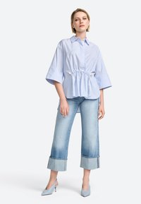 Chemise rayée bleue avec taille à cordon, associée à un pantalon en jean clair coupé avec des ourlets effilochés et des chaussures à talons hauts bleu pâle.