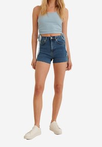 Mörkblå denimshorts med fransar, hög midja och sidodetaljer. Matchas med en ljusblå ribbad linne och vita sneakers.