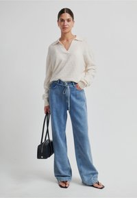 Krémový pletený svetr s výstřihem do V, doplněný světle modrými širokými džínovými kalhotami. Styl je doplněn černou kabelkou a černými sandály.