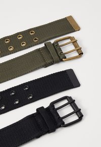 Three fabric belts: olive green, black with grommets, and solid black. Each features distinct buckles—metal, matte black, and antique finish.