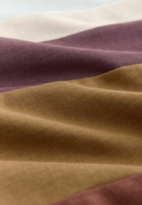 Gros plan sur un tissu doux à larges rayures horizontales en beige, violet atténué et jaune moutarde.