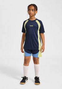 Marinblå sporttröja med limegröna detaljer tillsammans med blå och limefärgade shorts. Har rund halsringning, korta ärmar och svarta sneakers.