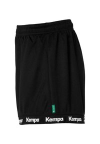 Shorts de sport noirs avec une taille élastique, présentant une bande au bas avec le logo "Kempa" en blanc et une étiquette d'accent vert sur le côté.