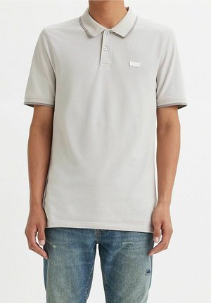 Lysegrå polo t-shirt med krave, tre knapper og kontrasterende teksturerede detaljer. Båret med blå slidte jeans.