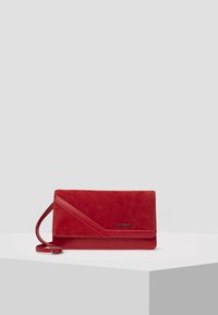 Pochette en daim rouge avec un design diagonal, dotée d'une bandoulière amovible et d'un accent de logo en métal. Texture lisse avec une forme élégante et moderne.