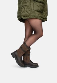 Botas altas de cuero y ante de color marrón con un acabado texturizado, que cuentan con cordones, un zipper lateral y una suela de tracción robusta.