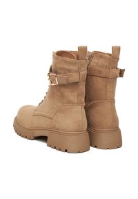 Světlé semišové kotníkové boty se zipem na zadní straně, masivní gumovou podrážkou a dekorativním páskem se zlatou sponou.