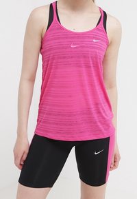 Žena v růžovém pruhovaném tílku přes černou sportovní podprsenku a černých cyklistických šortkách s růžovými postranními panely, vše označené logy Nike.